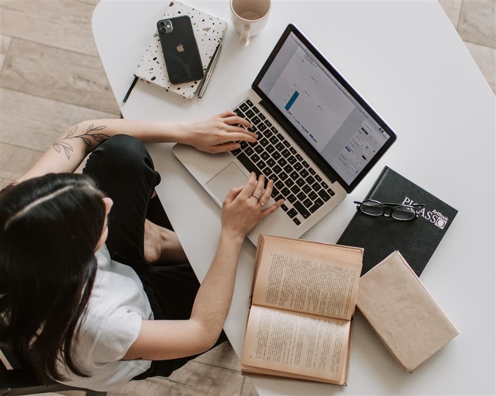  Person sitting at laptop working with books along side